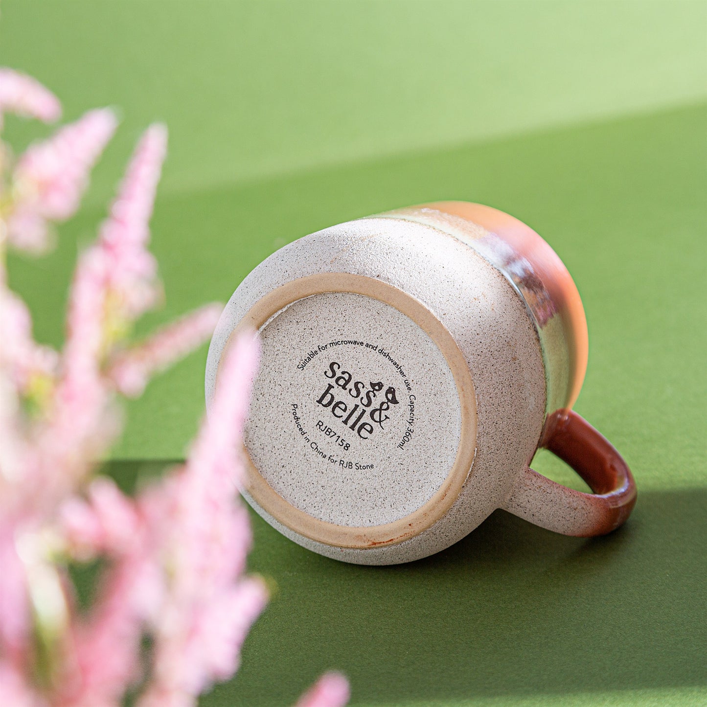 Ceramic mug with 'sas & belle' branding on a green background