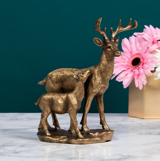 Bronzed deer and fawn figurine displayed on marble surface with pink flowers in the background – The Leonardo Collection home decor piece.